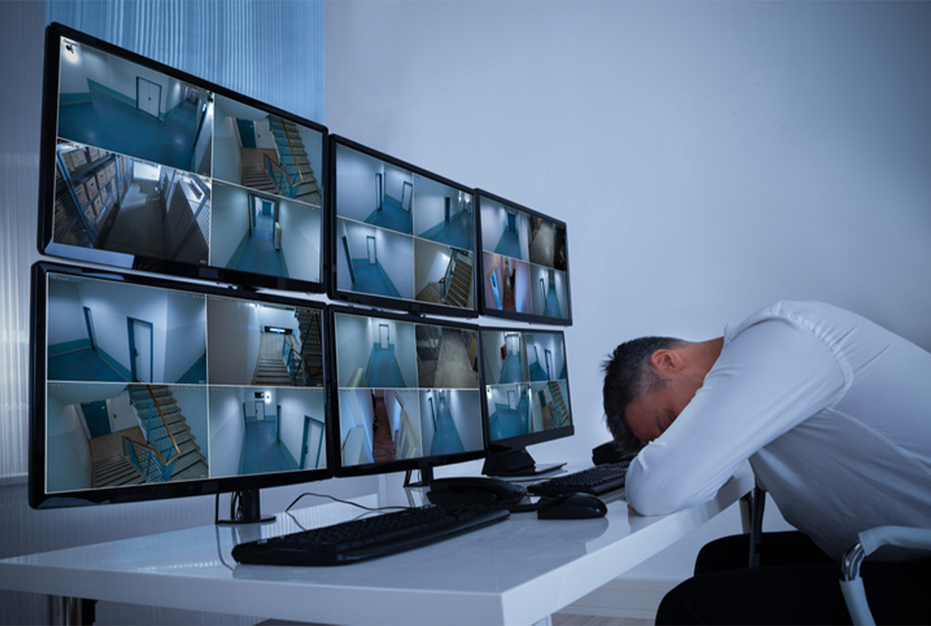 Security guard sleeping at his desk with security camera footage on screens