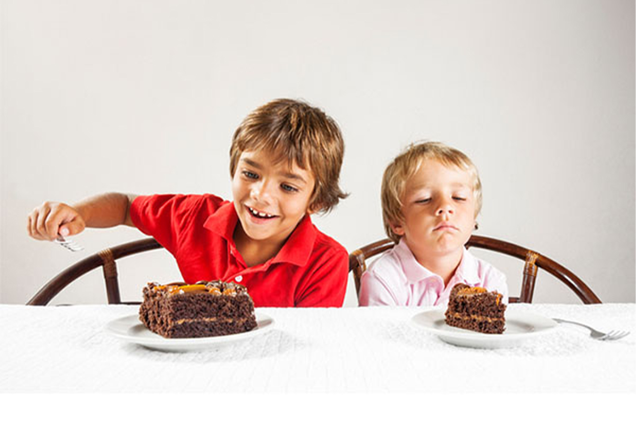 two boys eating cake, but one has a smaller slice